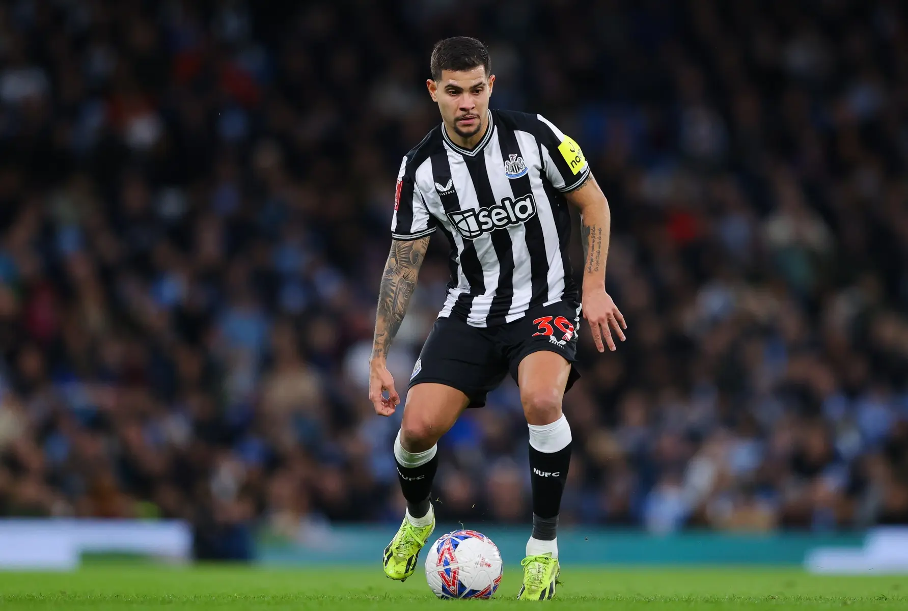 Bruno Guimaraes wearing Newcastle United kit, dribbling a soccer ball on the field.