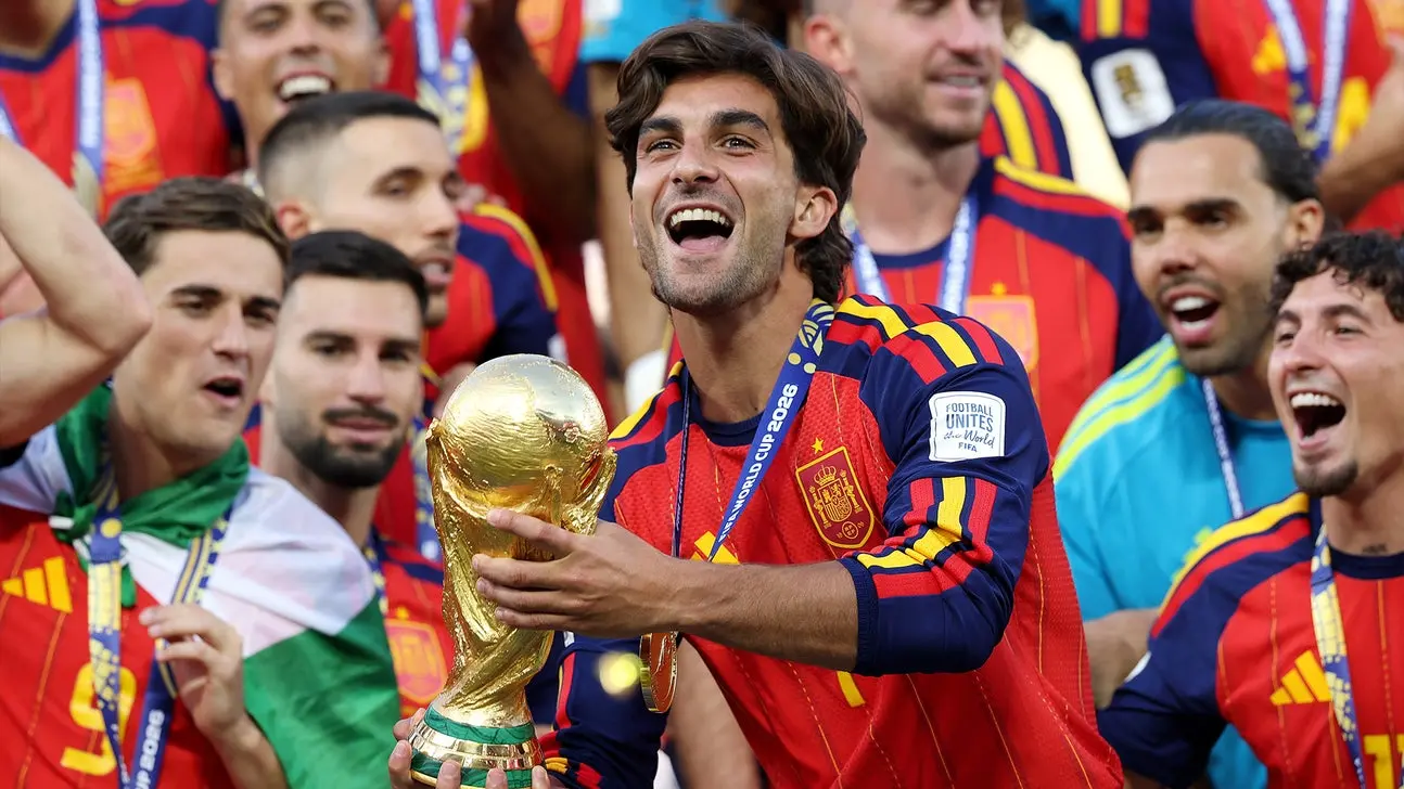 Ferran Torres celebrating with the FIFA World Cup trophy surrounded by teammates.