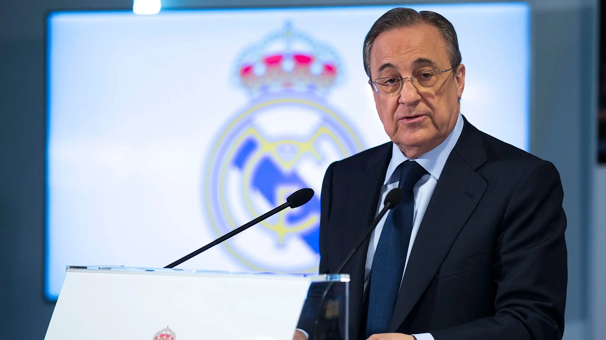 Florentino Perez speaking at a podium with Real Madrid logo in the background.