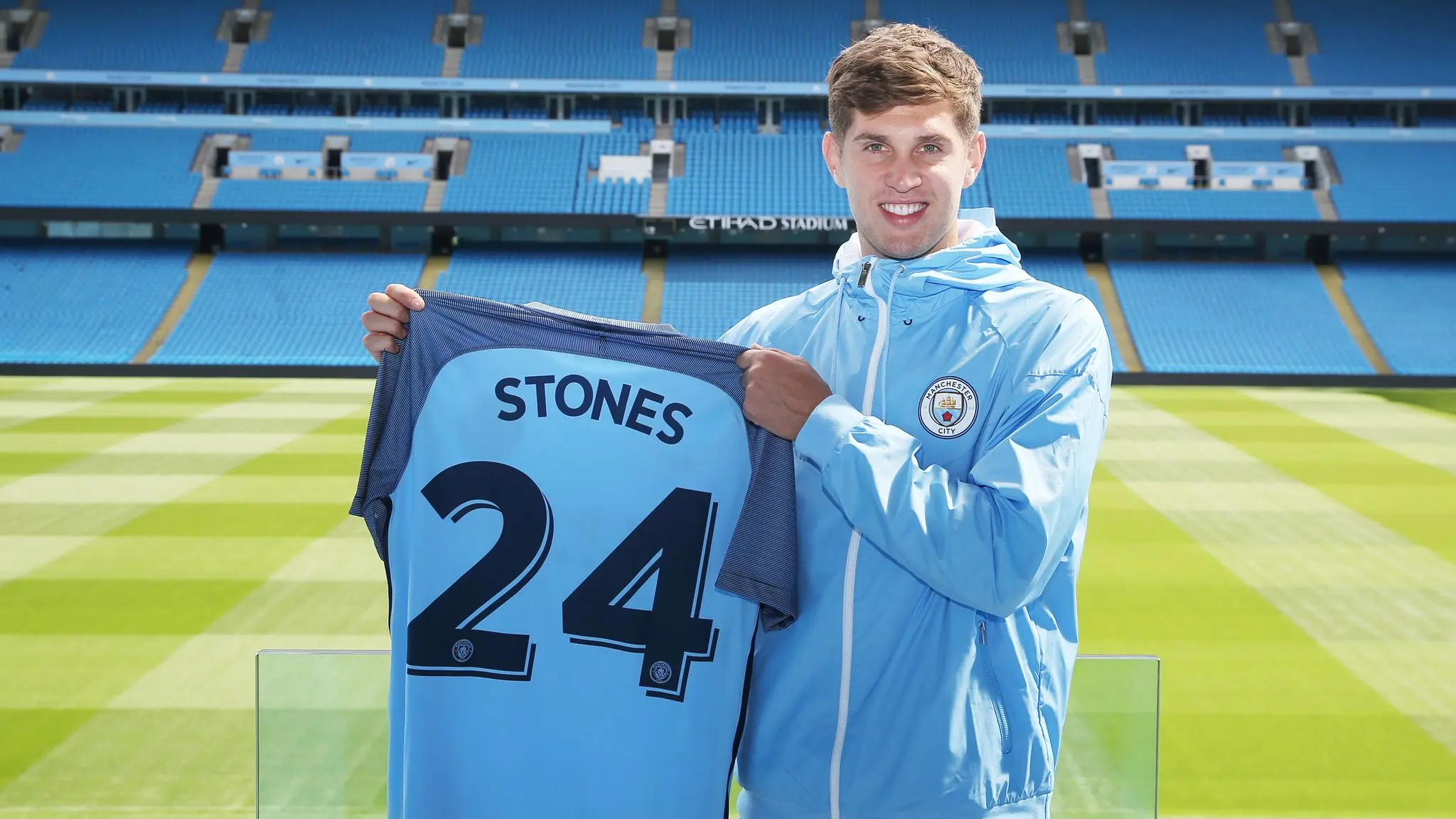 John Stones holds Manchester City jersey at Etihad Stadium.